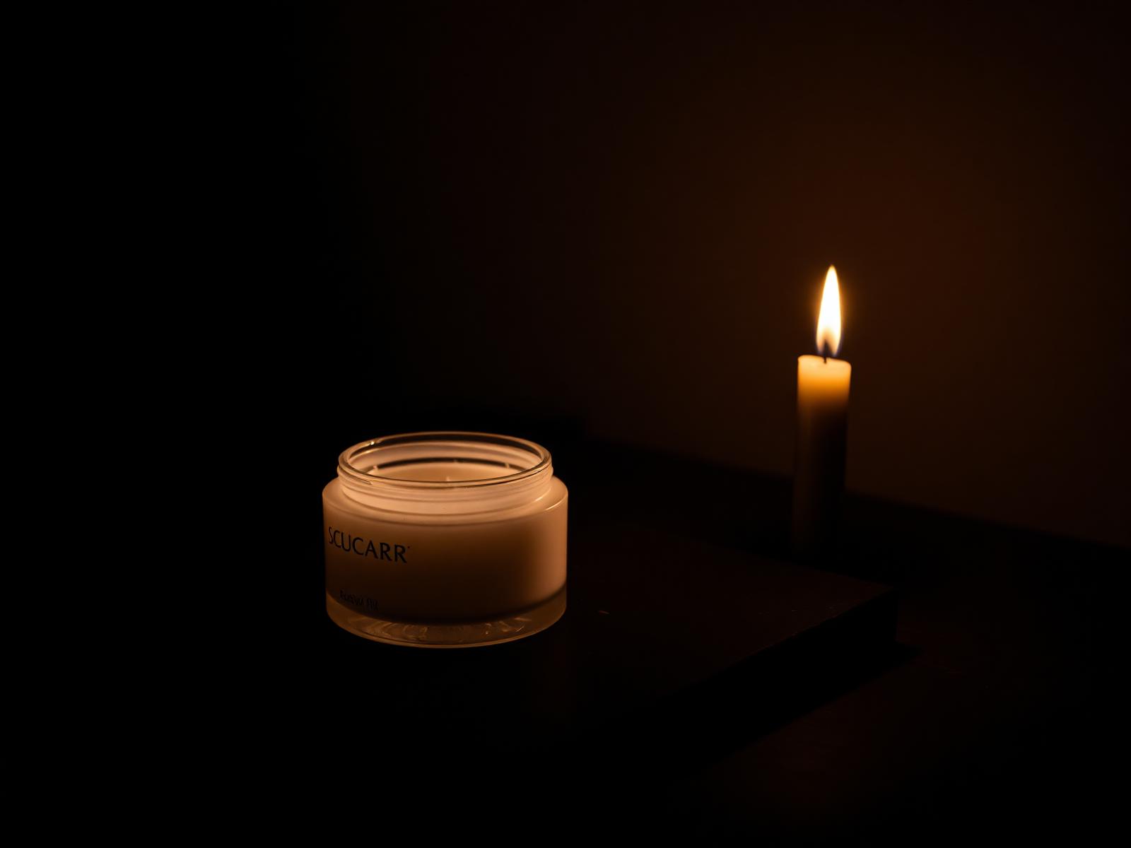Candlelit jar of cream resting on a dark stone surface in soft golden light.